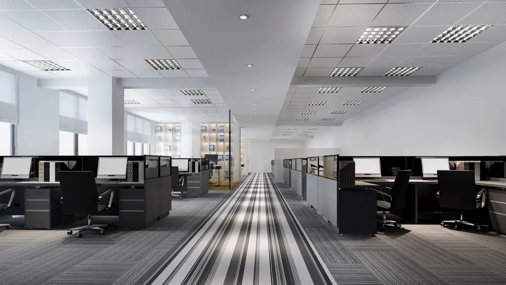 Office interior with rows of desks, computer monitors, and chairs.
