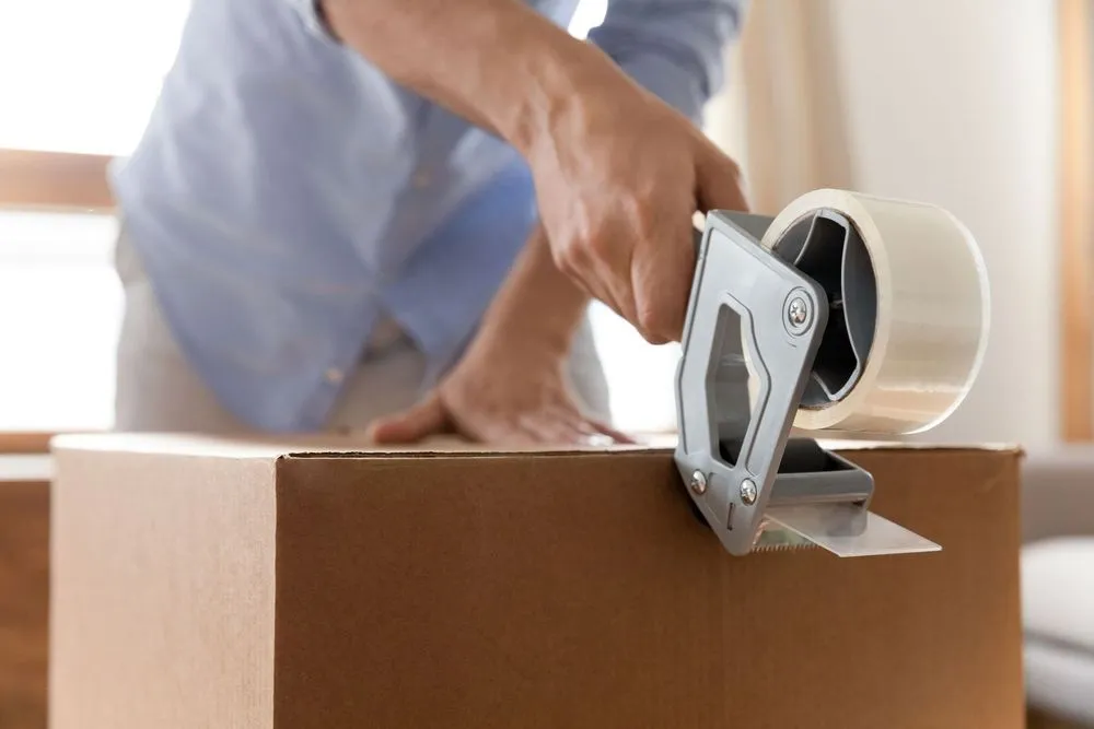 Person sealing a cardboard box with packing tape.